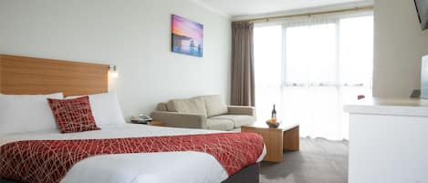 A hotel room with a large bed, a sofa, a small table, and a window with curtains.