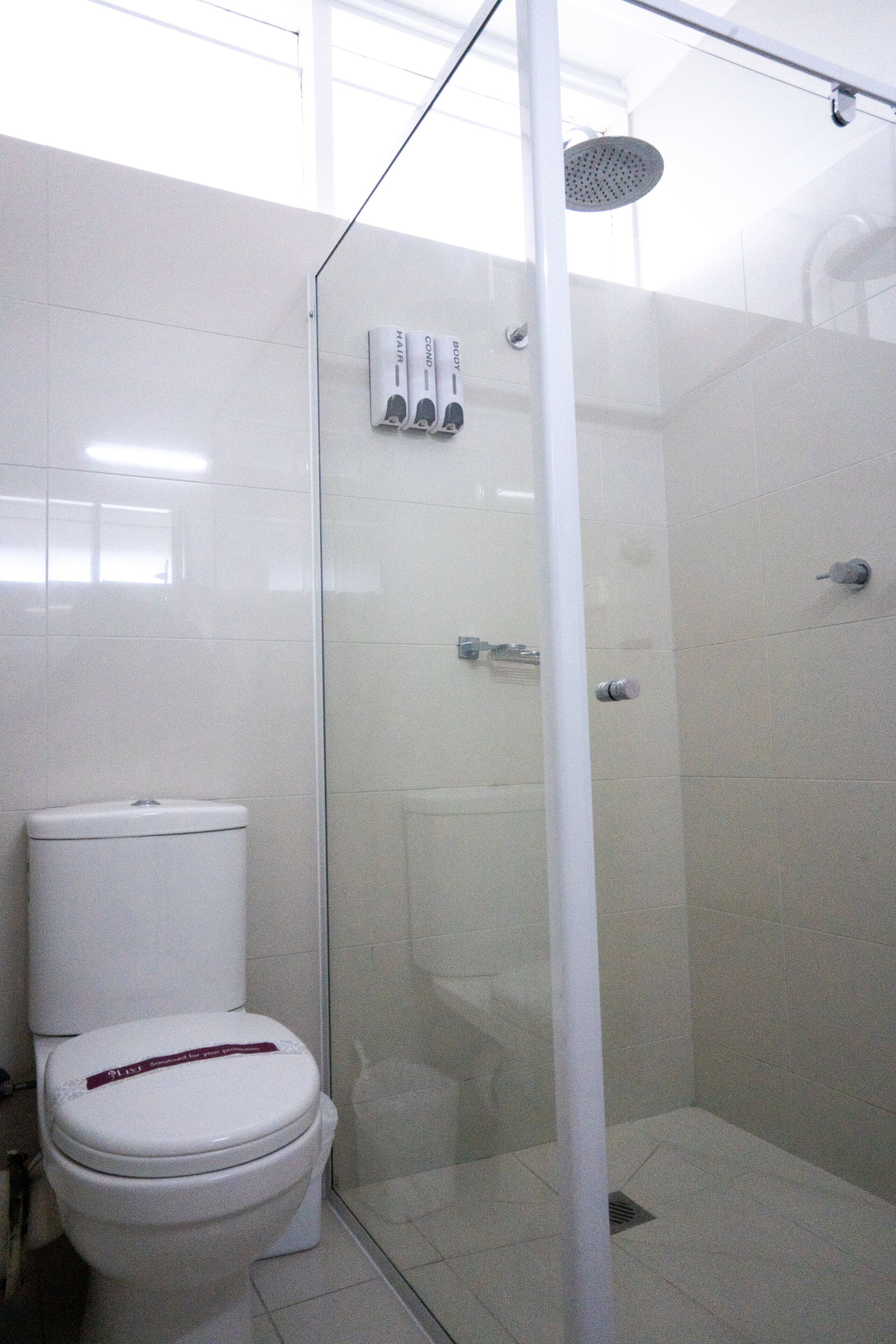 A bathroom with a toilet, a glass-enclosed shower, and a wall-mounted hairdryer.