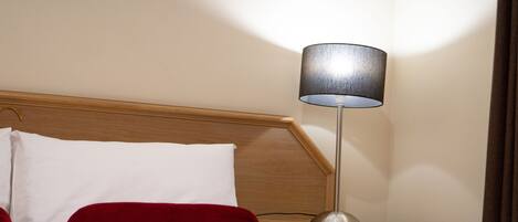 A neatly made bed with white and red bedding, a wooden headboard, and a bedside lamp on a wooden nightstand.