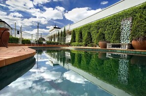A swimming pool with a clear reflection, surrounded by a well-maintained hedge and a modern building with a flat roof. - Admiralty Inn (Geelong)