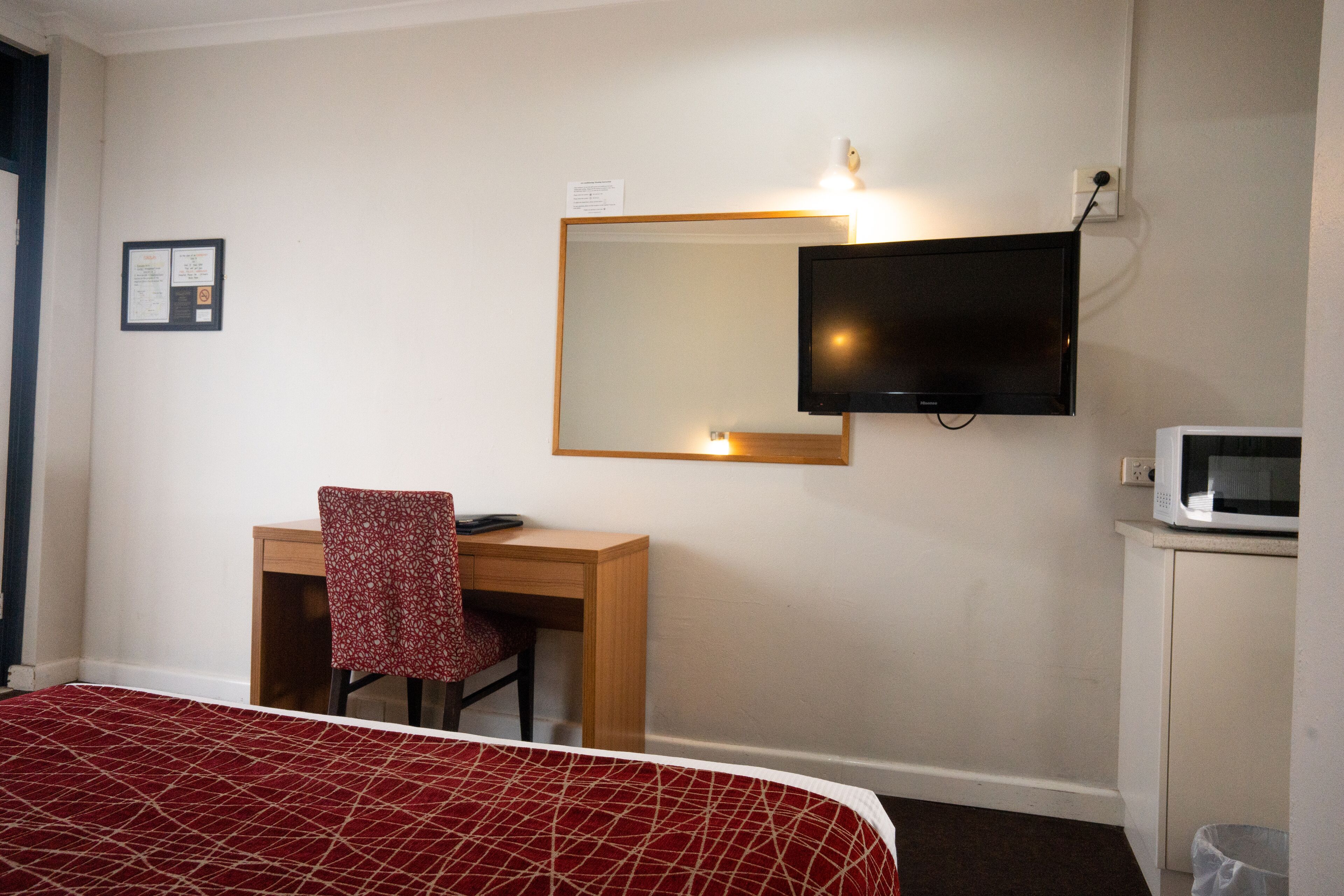A hotel room with a bed, a desk with a chair, a television mounted on the wall, and a microwave on a cabinet.