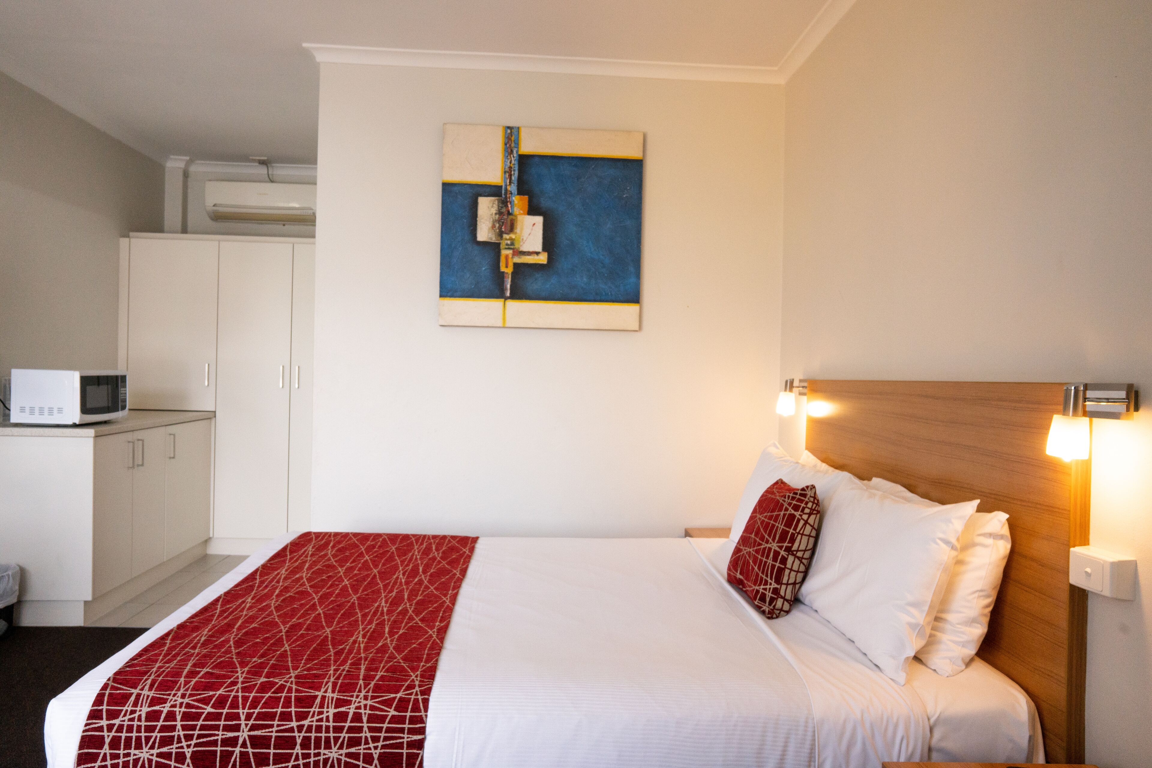 Habitación de hotel con cama, microondas, armario y una obra de arte colgada en la pared.