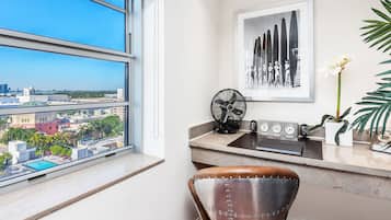 A modern room with a large window, a desk with a fan, a chair, a clock, and a framed artwork.