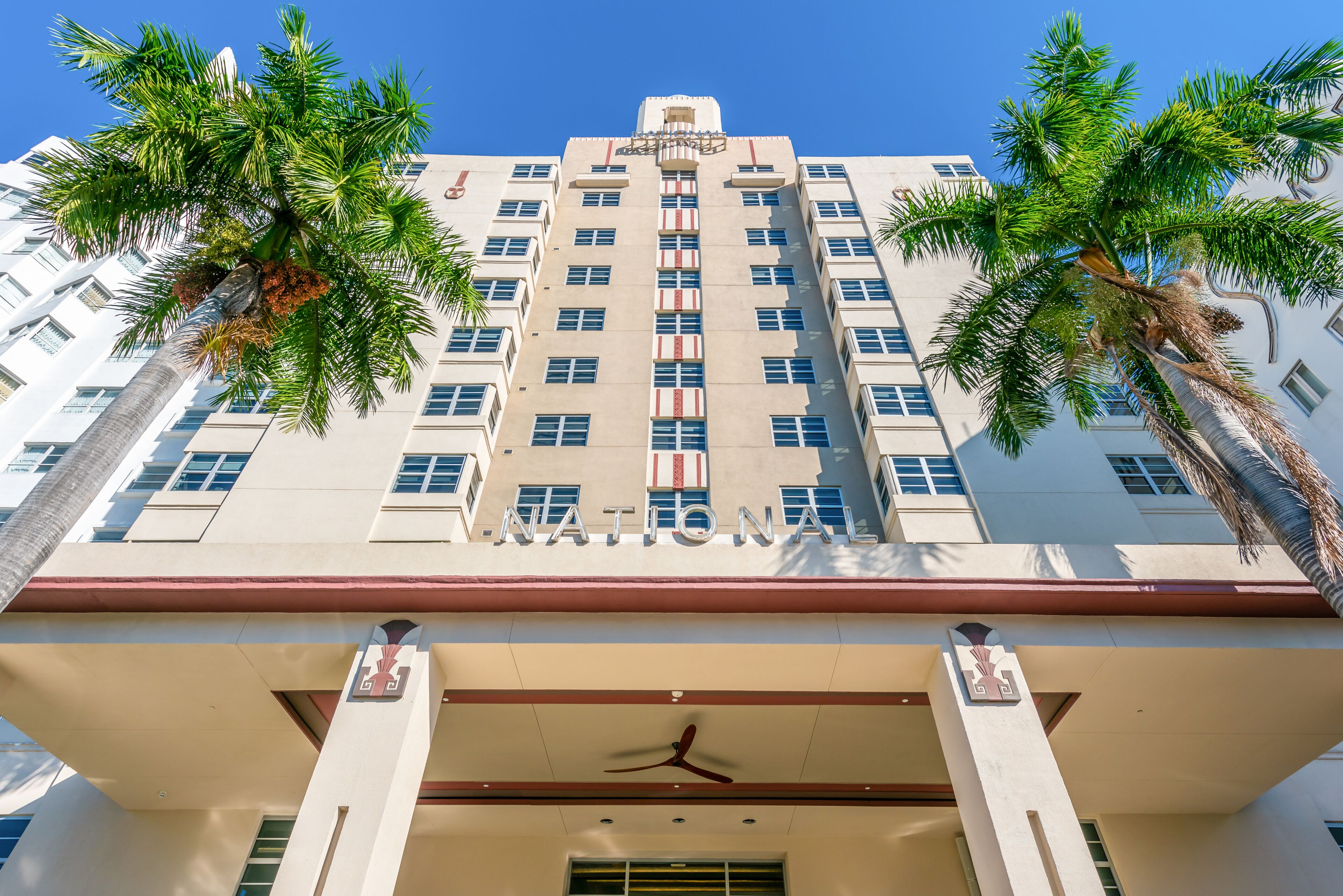 A tall, white building with the word "NATIONAL" on the facade, palm trees, and a central entrance with a fan.