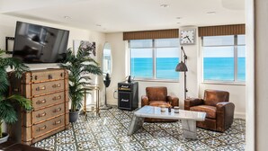 A spacious living room with a large window offering a view of the ocean, a vintage suitcase, a Marshall amplifier, and a leather armchair.