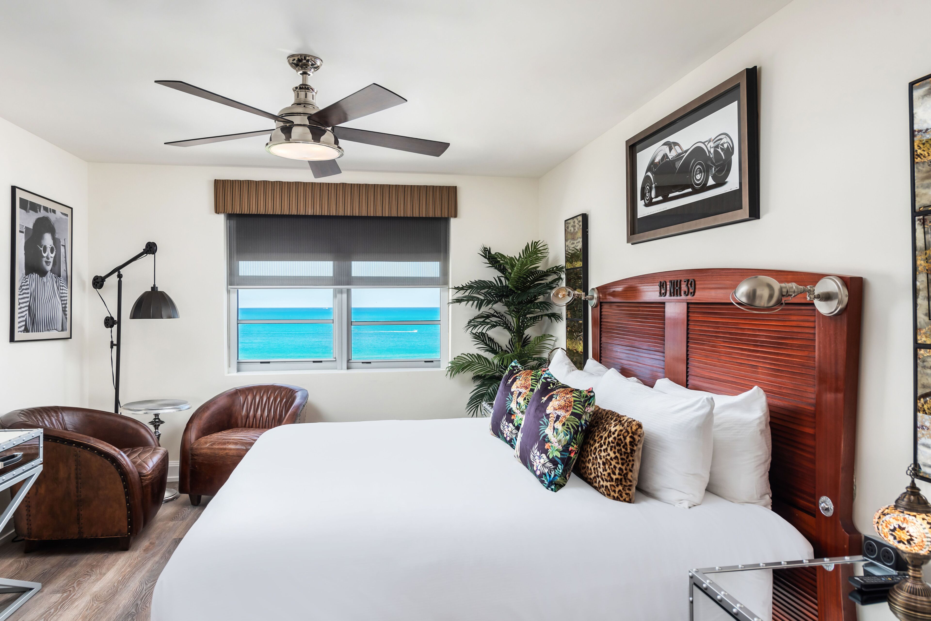 A spacious bedroom with a large bed, a ceiling fan, a view of the ocean, a wooden headboard, and a desk with a chair.