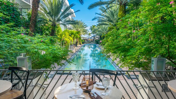 A poolside dining area with tables and chairs, overlooking a swimming pool surrounded by lush greenery. - The National Hotel Miami Beach (Miami Beach)