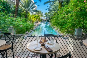 A poolside dining area with tables and chairs, overlooking a swimming pool surrounded by lush greenery.