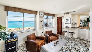 A living room with a view of the beach, leather chairs, a table with drinks, and a kitchen area with bar stools. - The National Hotel Miami Beach (Miami Beach)
