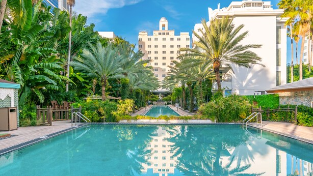 A swimming pool surrounded by palm trees and a large building in the background.