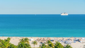 A beach with a cruise ship in the distance, palm trees, and beach umbrellas. - The National Hotel Miami Beach (Miami Beach)