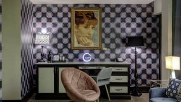 Una sala moderna con un estampado de cuadros en la pared, techo floral, un escritorio con lámpara, una silla y una mesa de centro redonda.