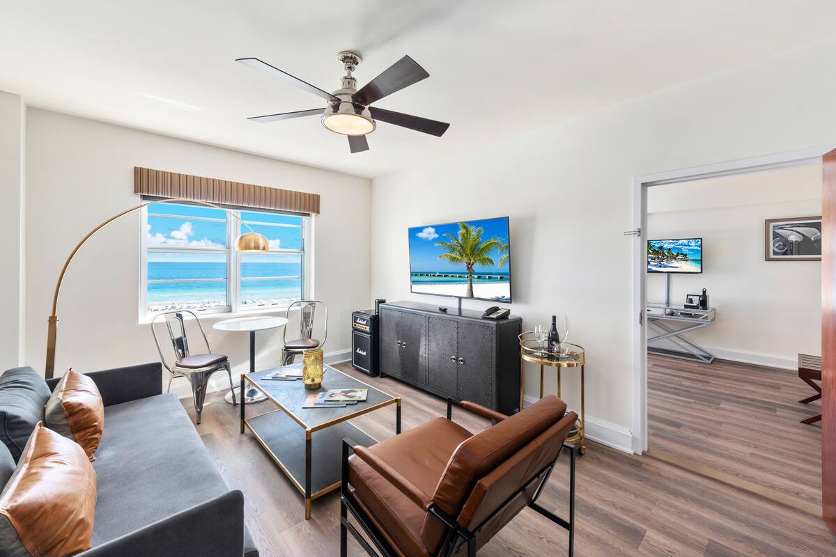 A modern living room with a view of the ocean, a ceiling fan, a TV, and a dining area.