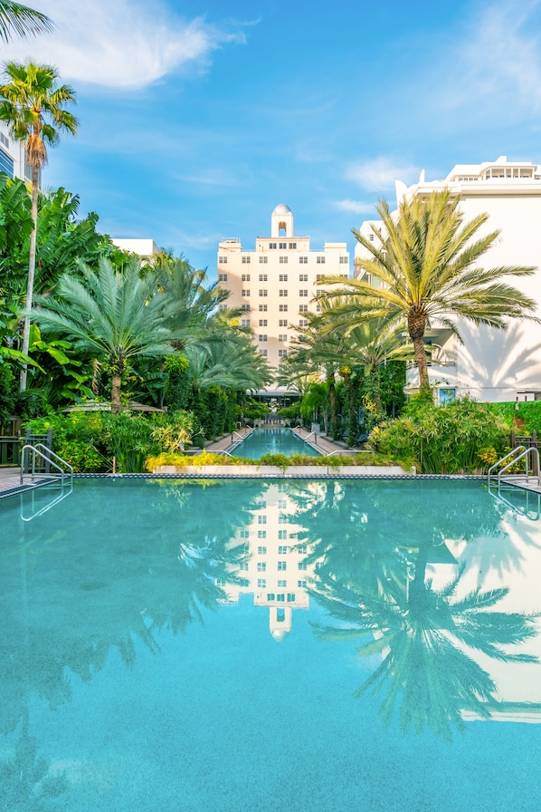 A swimming pool surrounded by palm trees and a building with a dome in the background.