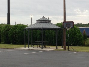 Relax in the serene gazebo-style pavilion surrounded by lush greenery and a basketball hoop.