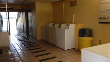 A laundry room with a washing machine, dryer, and a trash can.