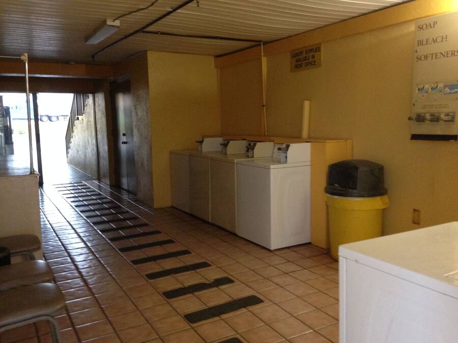 A laundry room with a washing machine, dryer, and a trash can.