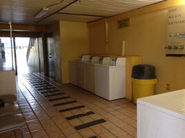 Un cuarto de lavandería con lavadora, secadora y un bote de basura.