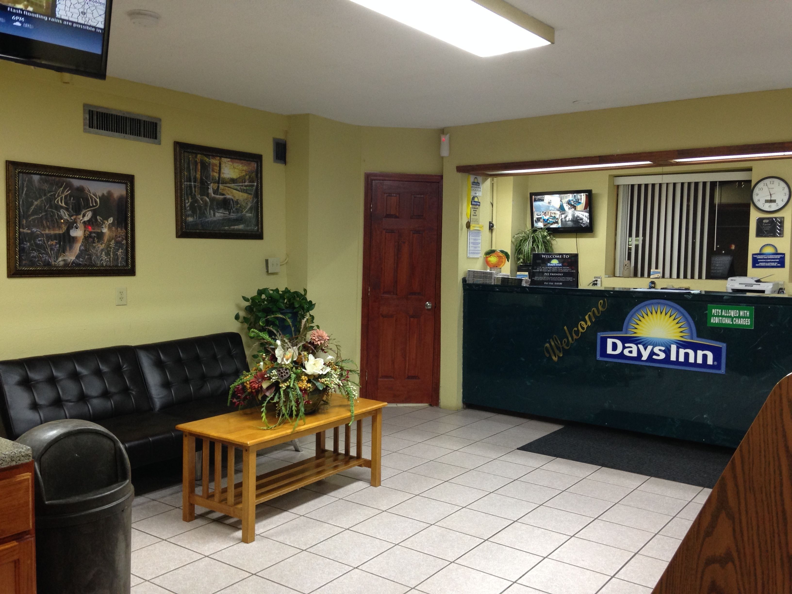A reception area with a Days Inn sign, a wooden bench with a floral arrangement, a black leather couch, and framed artwork on the walls.