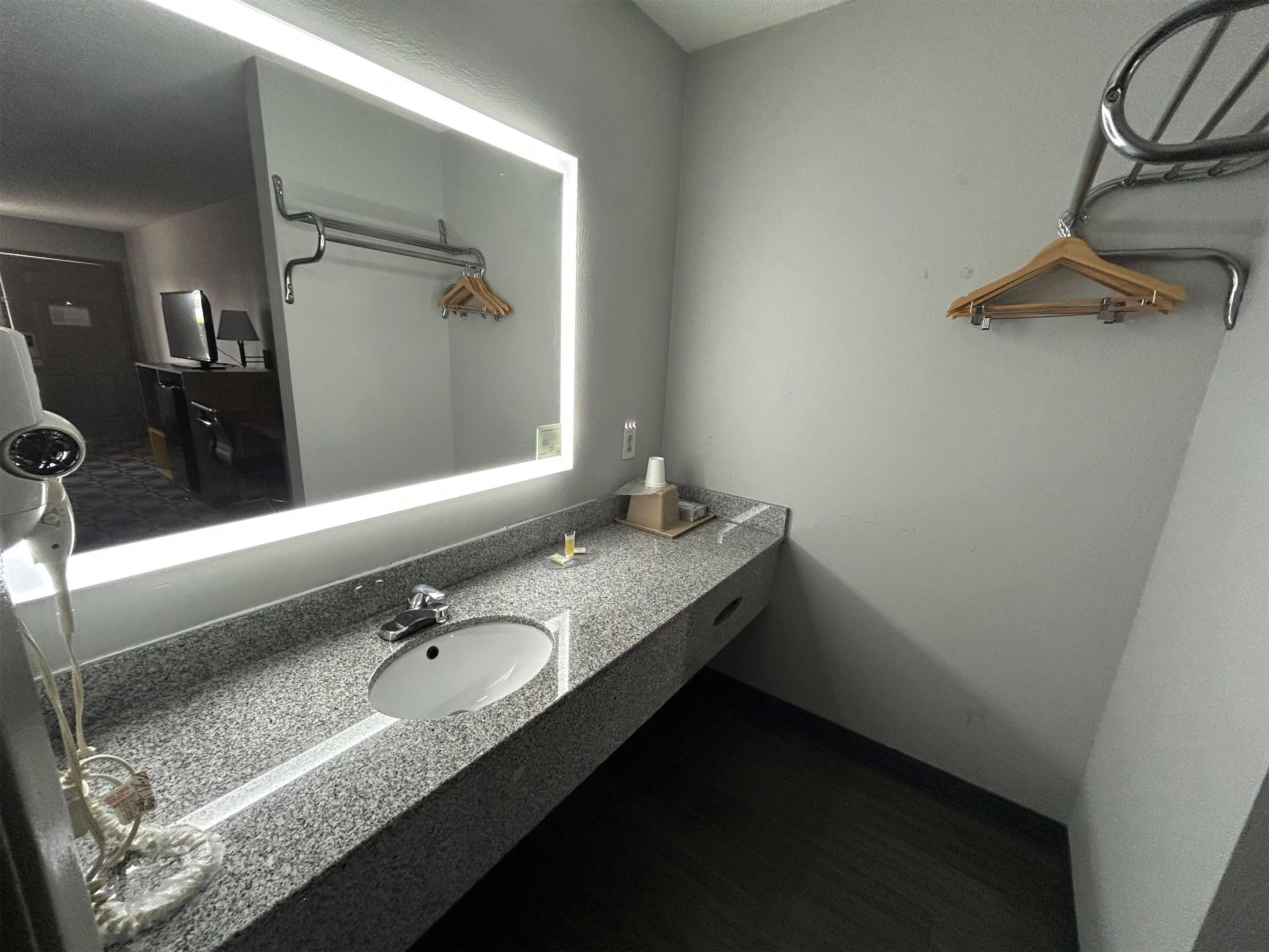 A modern bathroom with a granite countertop, a white sink, a large mirror, and a towel rack.