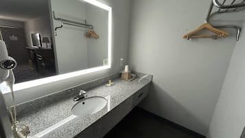 Un baño moderno con encimera de granito, un lavabo blanco, un espejo grande y un perchero para toallas.