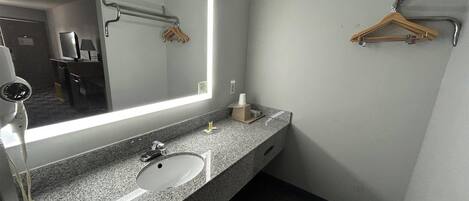A modern bathroom with a granite countertop, a white sink, a large mirror, and a towel rack.