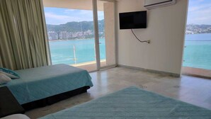Habitación de hotel con dos camas, televisión y vista al mar.