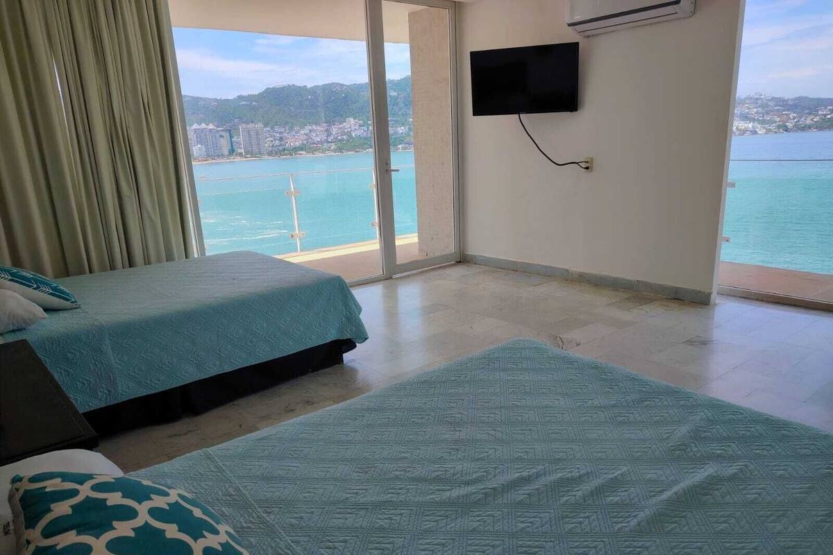 A hotel room with two beds, a TV, and a view of the sea.