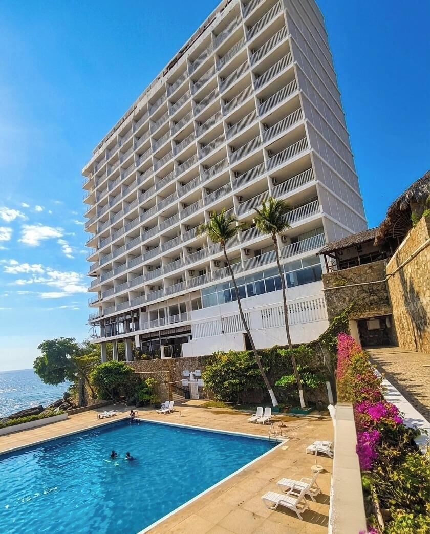 Un hôtel de grande hauteur doté d’une piscine, de palmiers et offrant une vue sur l’océan.