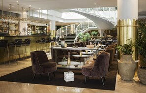 Un área de bar moderna con una escalera espiral, diferentes disposiciones de asientos y una barra con vasos.