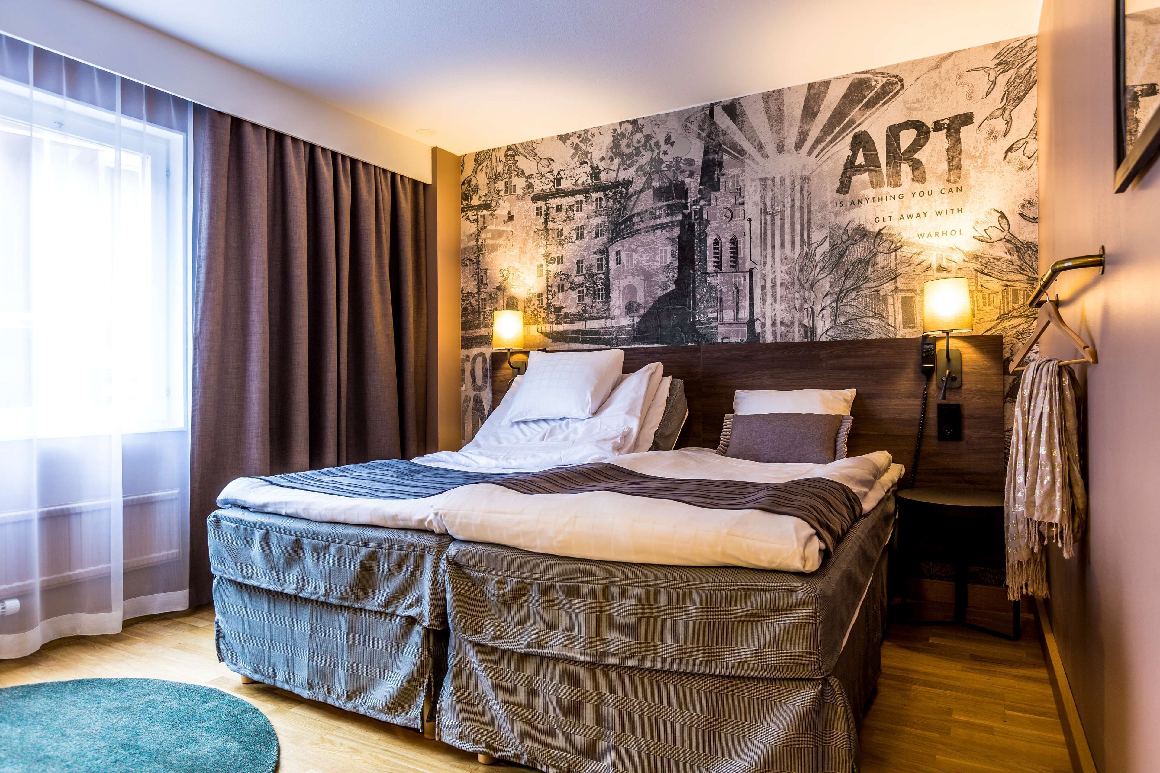 Una cama bien tendida con un cabecero, un tapiz de pared grande y dos lámparas de noche.