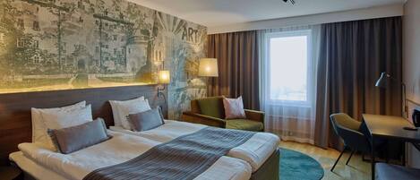 A hotel room with a large bed, a desk, a chair, and a view of the city through the window.