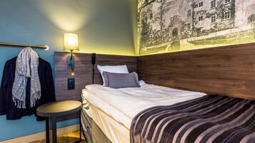 A hotel room with a bed, a nightstand, a lamp, a wall-mounted phone, and a towel rack.