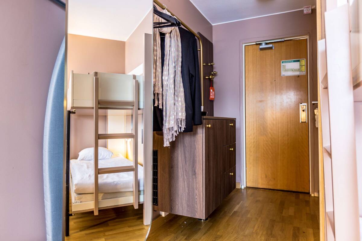 A room with a bunk bed, a wooden wardrobe, and a door with a fire safety sign.