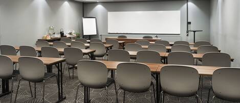 A conference room with a projector screen, a whiteboard, and a table with chairs.