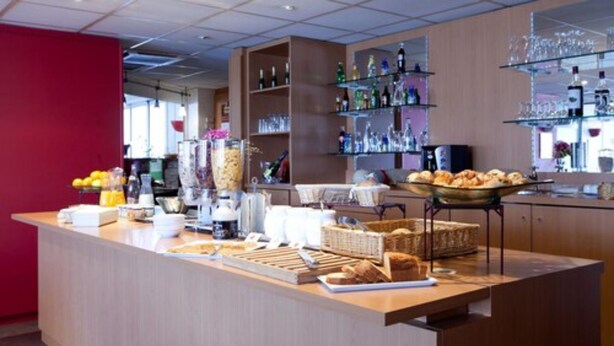 Un comptoir de petit-déjeuner proposant divers aliments et boissons, une machine à café, ainsi que des étagères remplies de bouteilles et de verres.