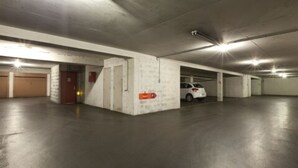 Un parking à plusieurs niveaux, avec des planchers et des murs en béton, où une voiture blanche est garée dans l’une des places disponibles.