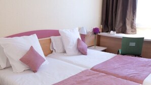 Une chambre d’hôtel avec deux lits, chacun agrémenté de draps blancs et roses, un bureau avec une chaise et une fenêtre avec des rideaux.