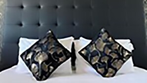 Une chambre d’hôtel avec une tête de lit capitonnée, deux coussins à motifs et des tableaux encadrés accrochés au mur.