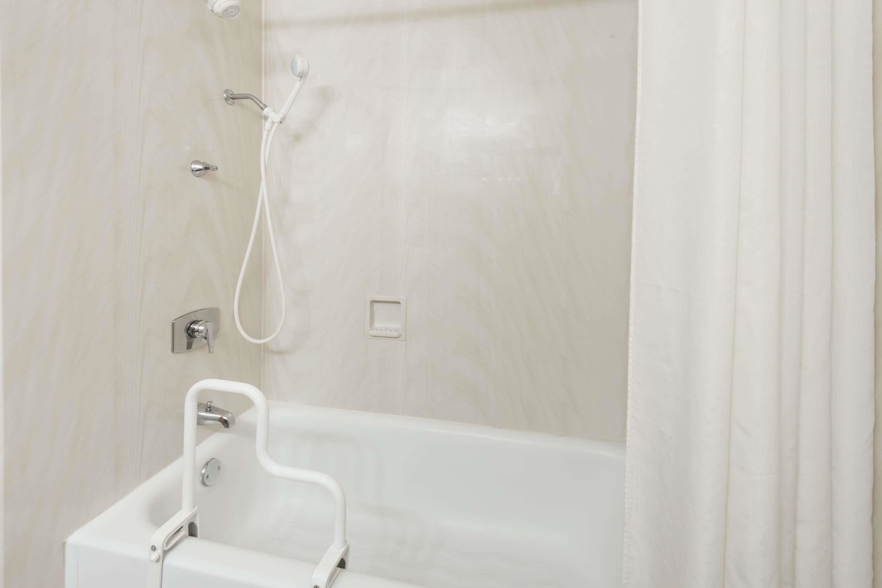 Un baño con una bañera blanca, un cabezal de ducha y un pasamanos.