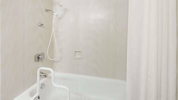 Un baño con una bañera blanca, un cabezal de ducha y un pasamanos.