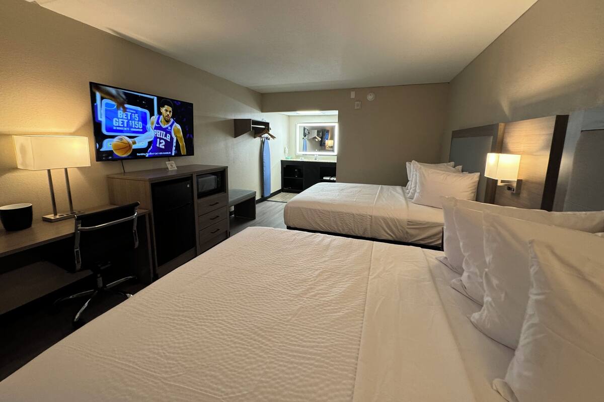 A hotel room with two beds, a desk with a computer, a TV, and a window with a view of the city.
