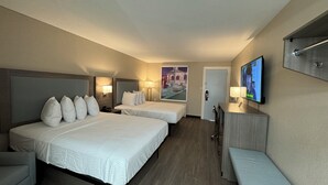 Habitación de hotel con dos camas, un escritorio, un televisor y una puerta.