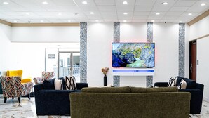 Un hall con una televisión de pantalla grande, dos sofás, sillas estampadas y suelo de mármol.