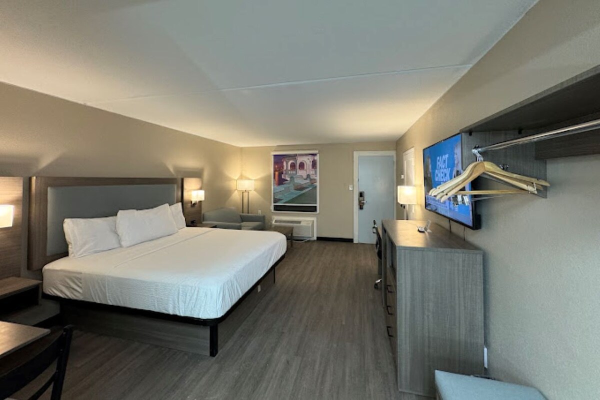 A hotel room with a large bed, bedside tables, a TV mounted on the wall, and a poster on the wall.