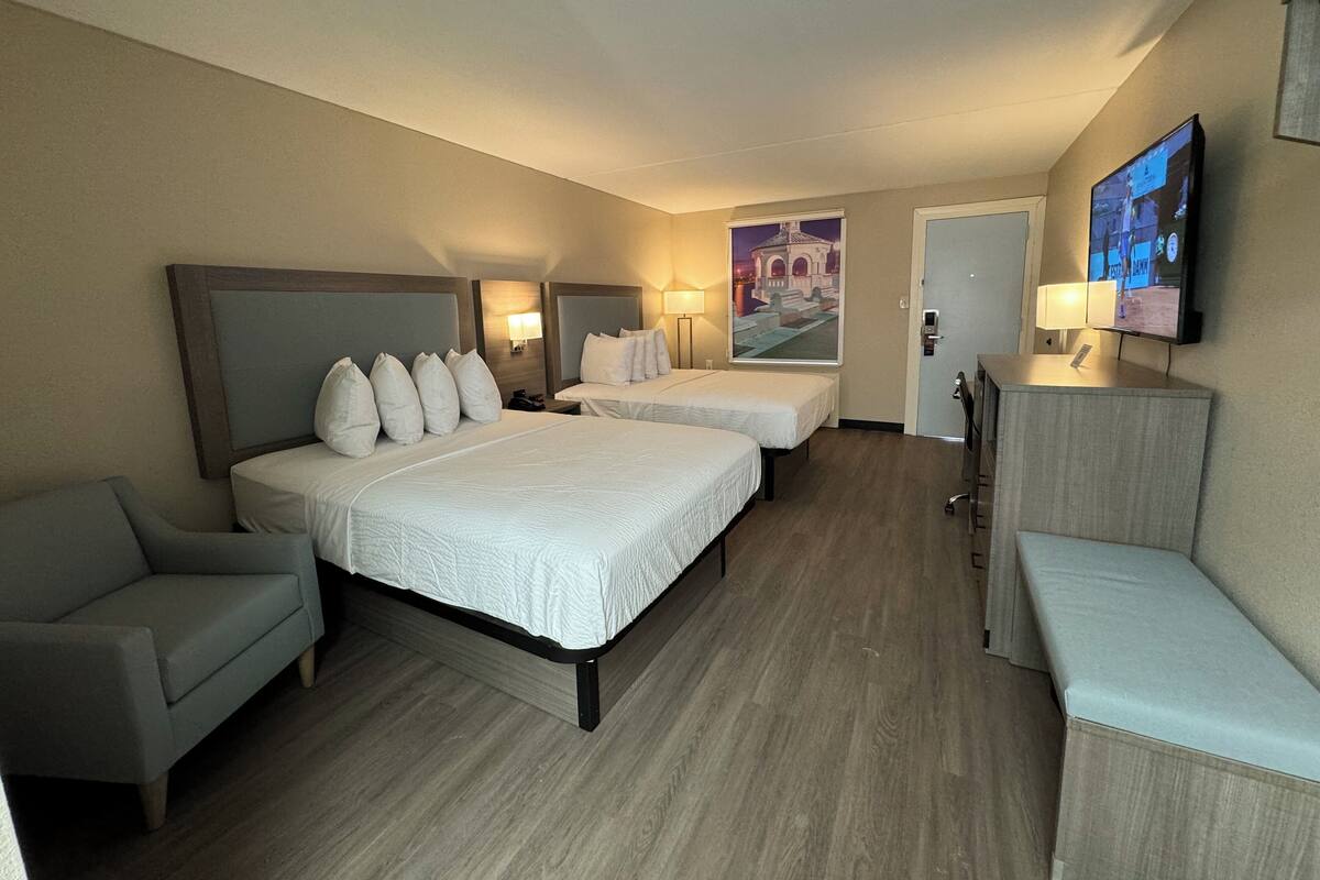 A hotel room with two beds, a sofa, a desk, and a TV.