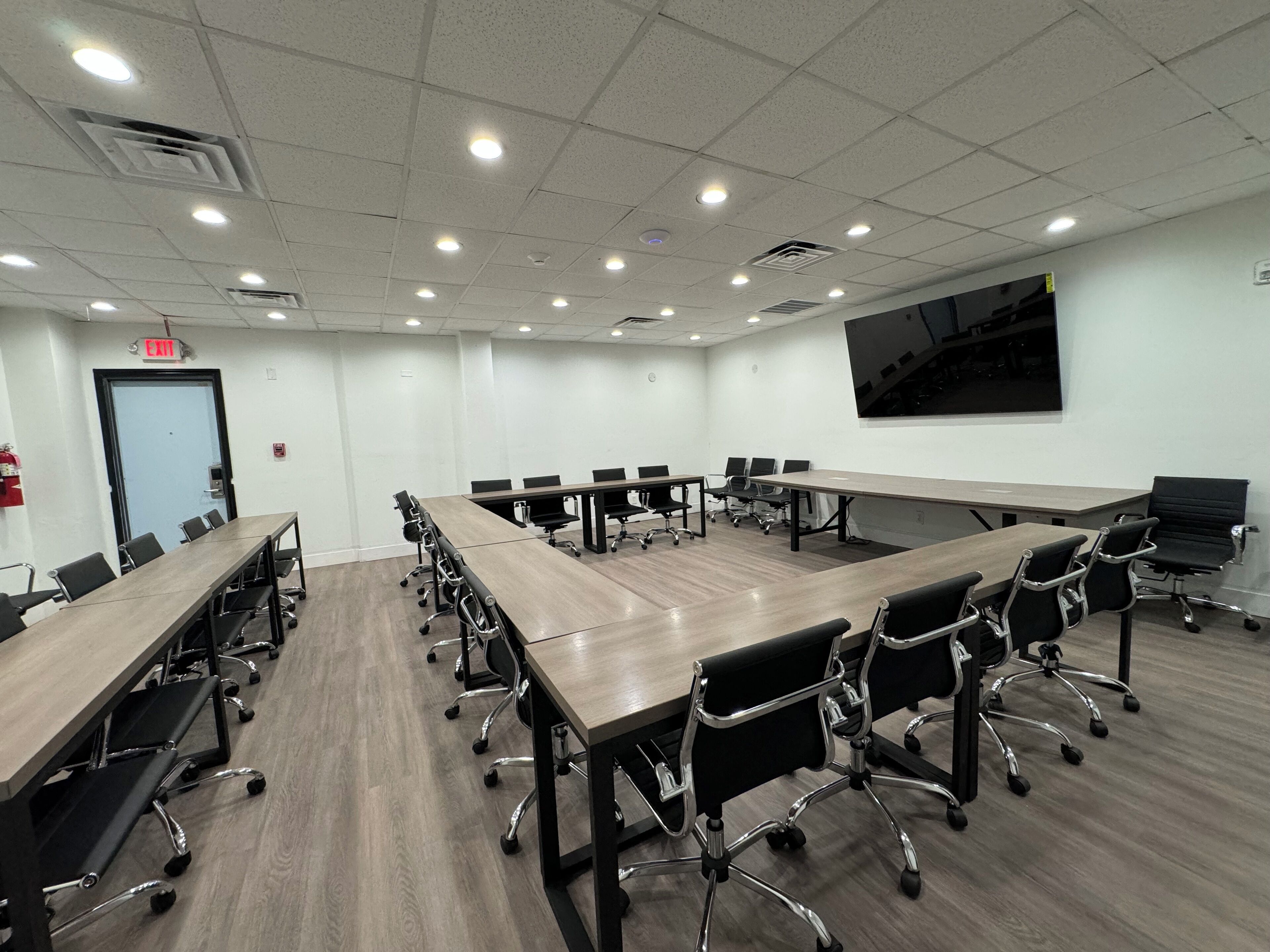 A conference room with long tables and chairs, white walls, and ceiling lights.