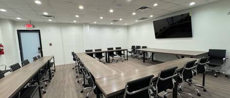 A conference room with long tables and chairs, white walls, and ceiling lights.