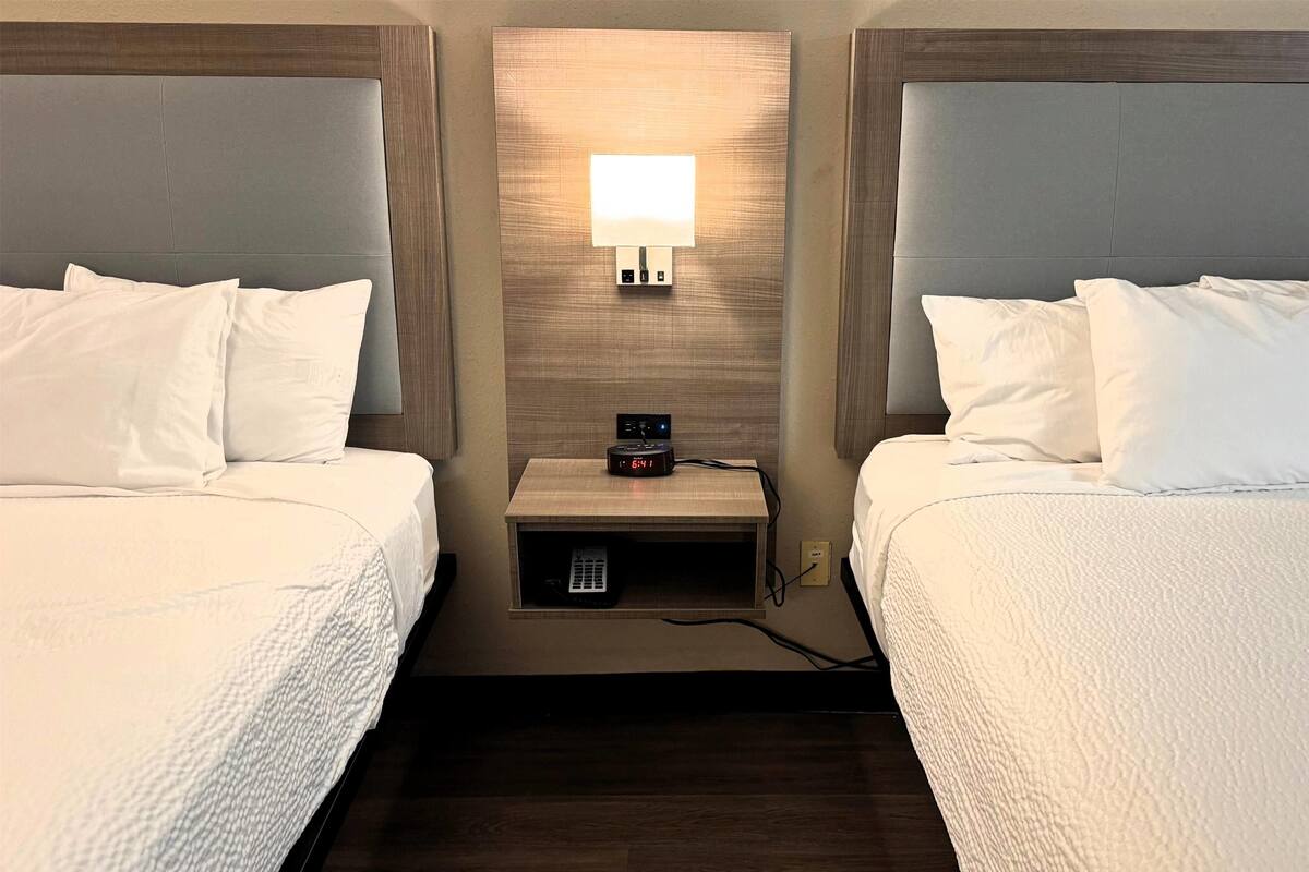 A hotel room with two beds, a bedside table with a lamp, and a clock.
