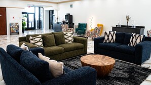 Un vestíbulo amplio con un sofá verde, un sofá azul y una mesa de centro de madera. Hay un mostrador de recepción con una máquina de café y una planta.